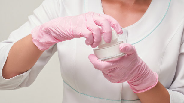 美容师打开一罐霜。美容师在美容院工作。化妆手段和护肤霜。手拿粉红手套和奶油罐图片下载