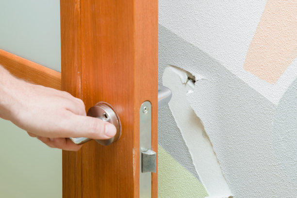 男人的手打开了门。因撞门而损坏的墙壁。问题和解决的概念。图片下载