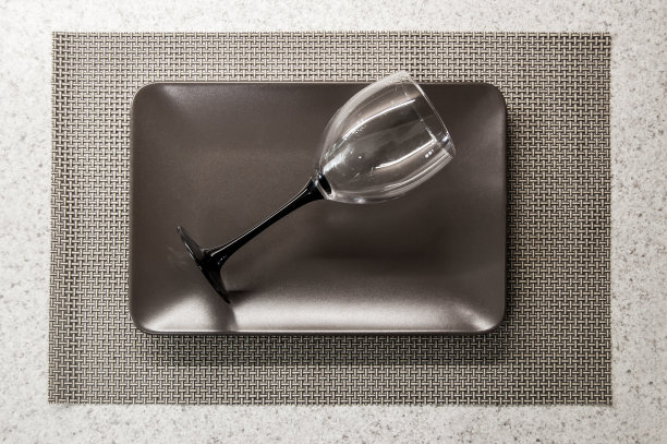 桌上棕色的盘子上放着一只空酒杯图片下载