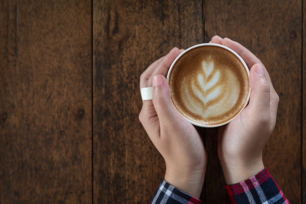女人手里拿着一杯咖啡在一张旧木桌上，俯视图图片下载