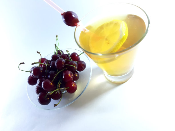 在透明容器中与水果一起饮用。柠檬和樱桃当点心。杯子里的黄色液体。现代设计照片。图片下载