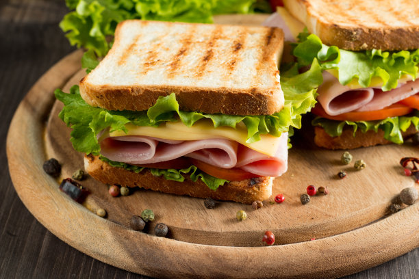 俱乐部三明治的特写照片。三明治与肉，火腿，意大利腊肠，沙拉，蔬菜，生菜，番茄，洋葱和芥末在新鲜的黑麦面包切片在木制背景。橄榄背景。图片下载