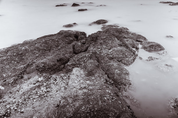 照片黑与白的长曝光摄影海浪在石头海滩水域边缘抽象的海洋背景。泰国。图片下载