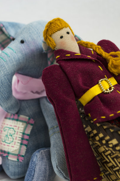 一个穿着彩色衣服的女性波浪娃娃坐在一个柳条篮子里，背景是白色的。登记的假期。室内手工制作的仙女娃娃。艺术和创造力。图片下载