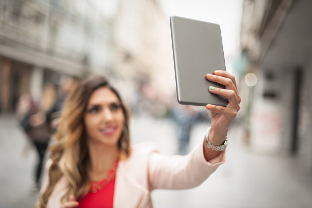 年轻女子在城市街道上用智能手机自拍图片下载