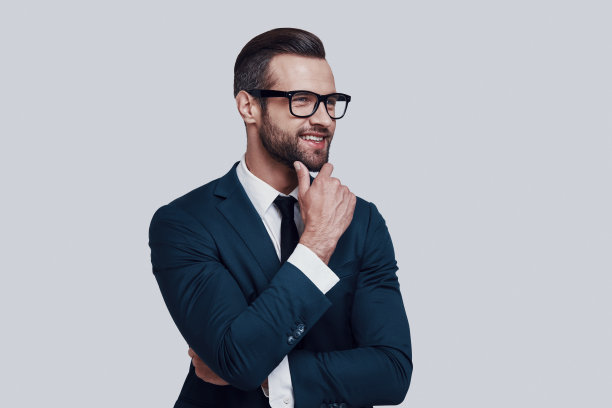 考虑业务。英俊的年轻人保持手在下巴和看向别处，而站在灰色的背景图片下载
