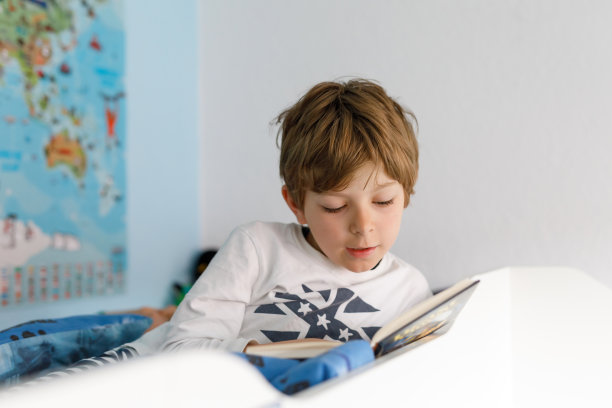 可爱的金发小男孩穿着睡衣在卧室看书图片下载