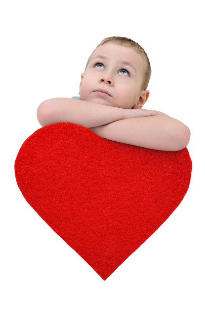 一个小男孩靠在一颗心上，抬起头来。恭贺情人节图片下载