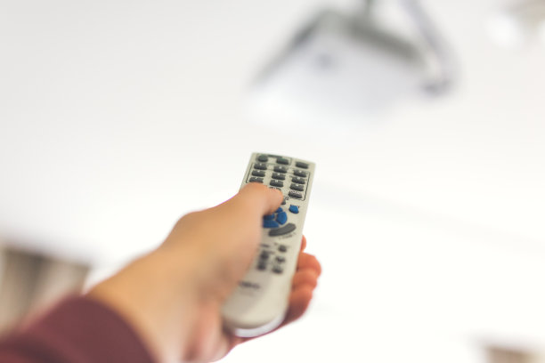 用遥控器打开办公室放映机的人。图片下载