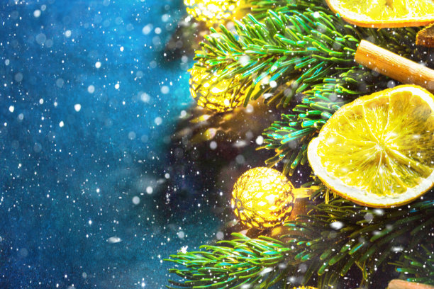 复古的圣诞新年贺卡。新鲜的蓬松的冷杉树枝，干燥的橙子片，肉桂枝，闪闪发光的金色花环，灯光雪在深蓝色的背景。附有版面的海报图片下载