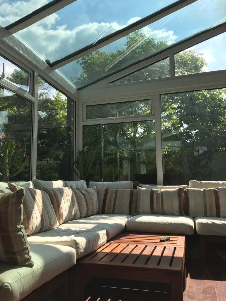 长方形的白色UPVC温室单间玻璃房间的图像，可以看到阳光明媚的花园景色，大的双层玻璃窗和带有自清洁窗格的玻璃屋顶/ l形的角落沙发放置温室家具，咖啡桌和电视电视遥控器图片下载
