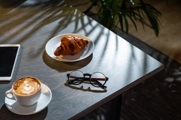 近距离的咖啡杯，羊角面包，眼镜和垫与空白屏幕。图片下载