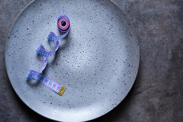 带卷尺的空盘子，在深色背景下有文字的位置。减肥食品。图片下载