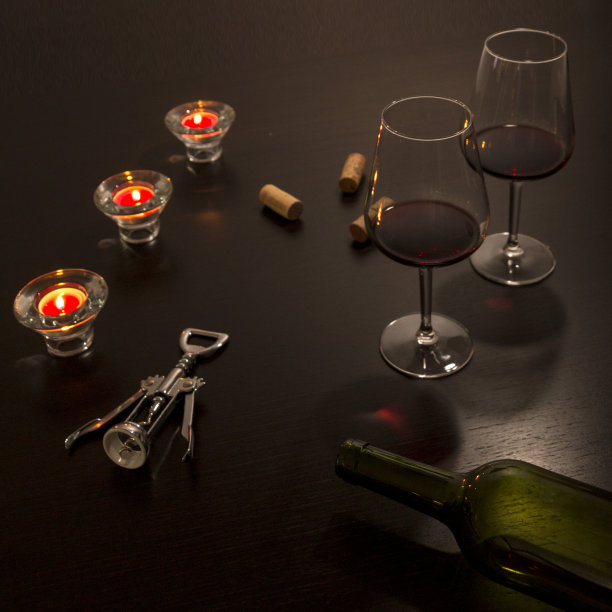 桌子上放着酒杯，上面有一个空瓶子，一个开瓶器和几支蜡烛照亮的暗色瓶塞。图片下载