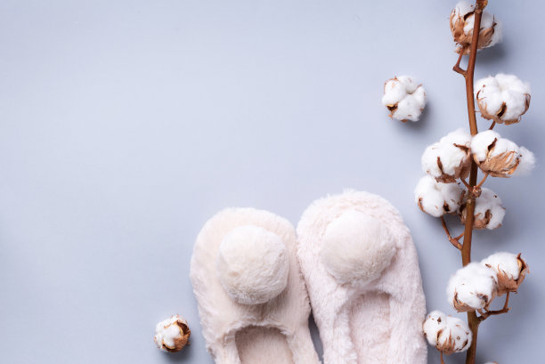 裸毛绒绒的家拖鞋与绒球和棉花花枝在灰色背景与复制空间。前视图。副本的空间。舒适的鞋子回家。温馨家居，水疗，身体护理理念图片下载