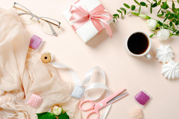 平躺，俯视图女性书桌与咖啡杯，鲜花，棉花糖，礼盒和线轴与丝带在粉红色的背景。节日家庭办公书桌概念，女性工作空间与女孩的配件图片下载