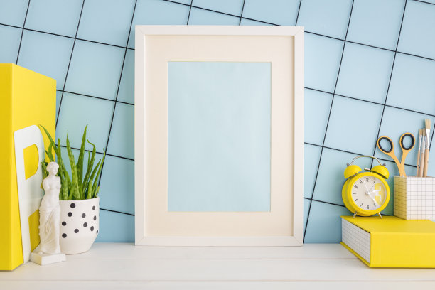 海报框在书桌上，学校文具，植物，笔记本靠在蓝色的墙上。模型。学校创造性的桌子。图片下载