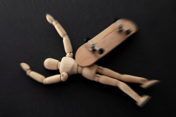 危险的伤害，危险的行为和极限运动概念主题与木制木偶和滑板的木材坠落到地上，受伤孤立在黑色的背景图片下载