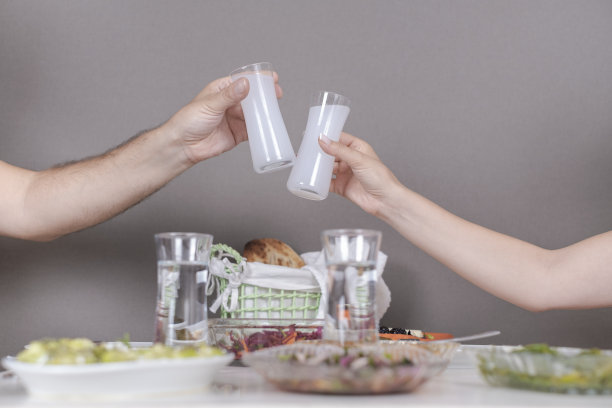 成年女人和男人的手臂与他们的raki杯在raki桌子上干杯/在灰色的背景上喝酒图片下载