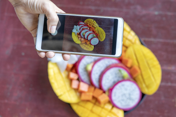 女人手拿手机拍照的热带水果。早餐的智能手机照片。甜甜的芒果，木瓜，火龙果。生素食素食健康食品图片下载
