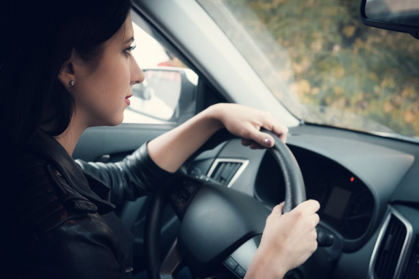 从车里看，在车里耐心等待的漂亮女人。可爱的黑发女孩坐着，握着方向盘向前看。女司机在车里等待，引擎已关闭。图片下载