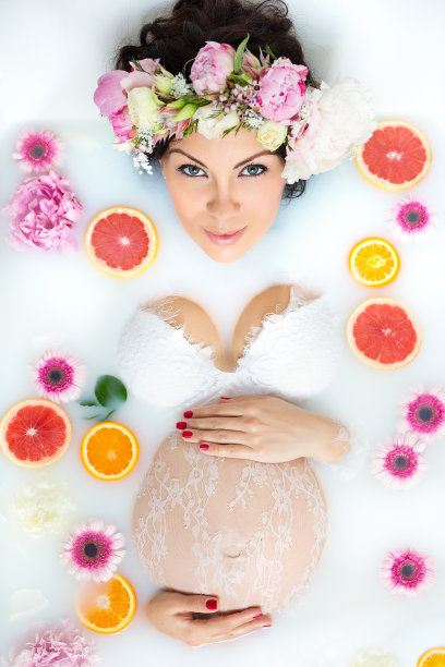美丽年轻的成年孕妇在牛奶浴与柠檬，葡萄柚和花图片下载