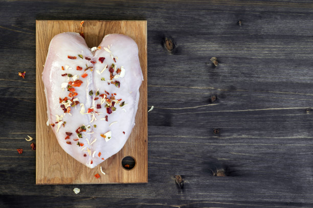 鸡胸肉和干蔬菜撒在竹砧板上，背景是乡村的木头。图片下载