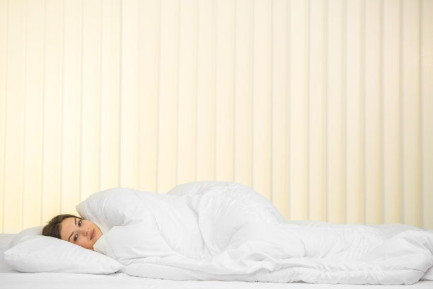 在一个百叶窗的背景上，睡在床上的年轻女子图片下载