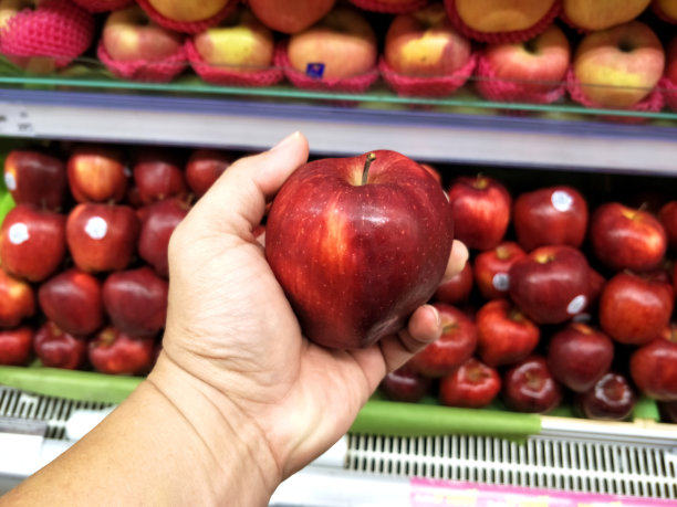 在超市里，男人用手挑选红苹果。图片下载