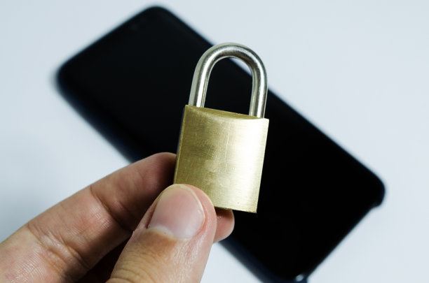 手机上的安全概念照片。一只手拿着一个锁住的锁和一个手机在背景中图片下载