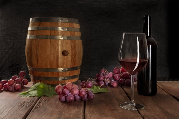 一杯红酒与一个瓶子，一个酒桶，葡萄，葡萄叶，在一个黑暗的乡村背景，低调的照片与复制空间图片下载