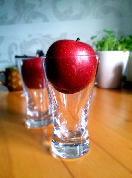 抽象的观点，闪亮的红苹果放置在高高的透明啤酒杯在递减的视角图片下载