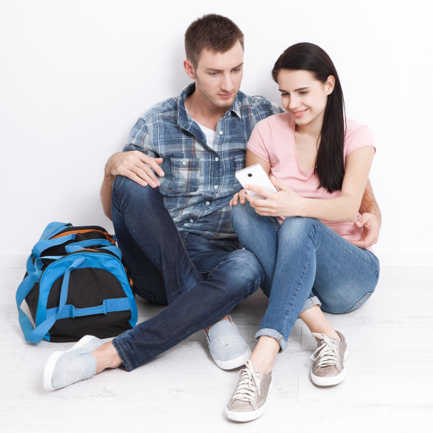 一男一女坐在一间新公寓里用智能手机。一对年轻夫妇选择结婚旅行。图片下载