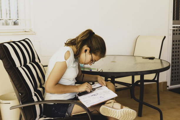 白人少女戴着眼镜戴着耳机听音乐，在阳台上写日记。图片下载