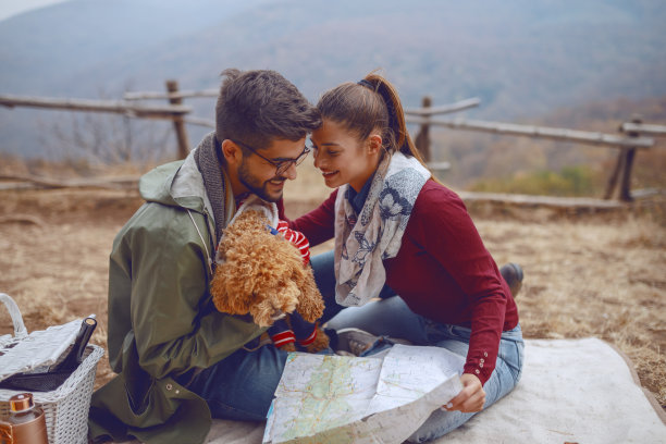 可爱的多文化夫妇坐在毯子上和他们的狗，调情和计划徒步旅行。秋天野餐概念。图片下载