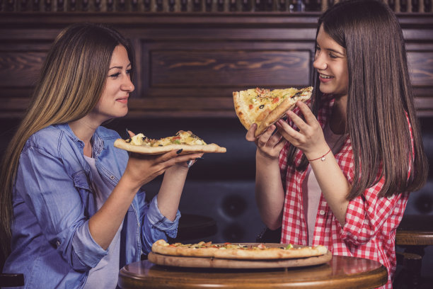 两个少女在餐厅享用美味的比萨图片下载
