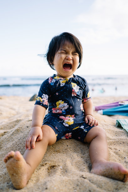 蹒跚学步的小女孩穿着泳衣坐在沙滩上哭泣图片下载