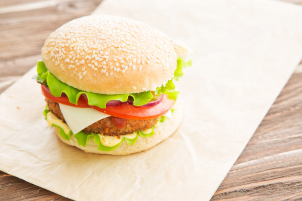 美味的快餐。芝士汉堡配上烤肉、芝士、番茄，放在牛皮纸上，贴在木板上。快餐模板。真实的照片。理想的广告图片下载