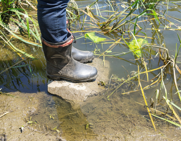 河边穿着胶靴的渔夫。阳光温暖的一天。身体的一部分，选择性聚焦。图片下载
