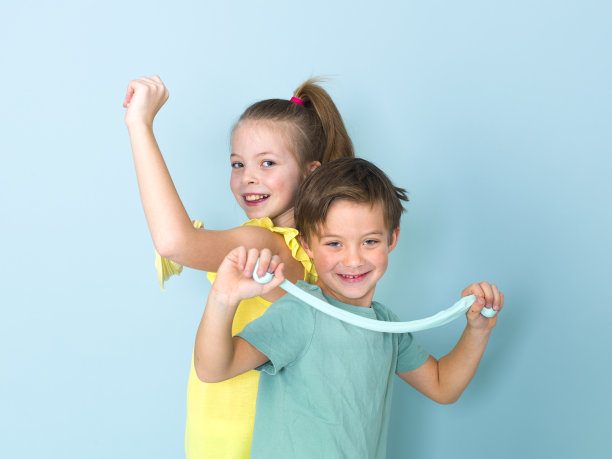 酷，漂亮的男孩和他的妹妹在蓝色背景前玩自制的黏液，玩得很开心图片下载