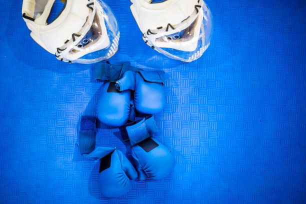 蓝色地板上放着两副蓝色战斗手套和两个白色头盔，上面戴着透明塑料穿孔口罩。空手道设备图片下载