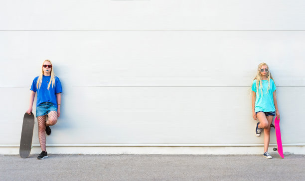 两个年轻的女滑板手靠在白色的墙上图片下载