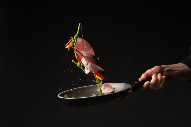 特写镜头。厨师在黑色背景的煎锅上用蔬菜煎鱼。水平的照片。海洋食品。健康食品。东方美食,禁止图片下载