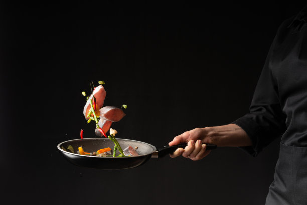 特写镜头。厨师在黑色背景的煎锅上用蔬菜煎鱼。水平的照片。海洋食品。健康食品。东方美食,禁止图片下载