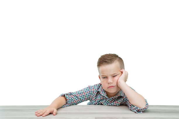 一个穿着格子衬衫的白人学龄男孩坐在桌旁睡着了图片下载
