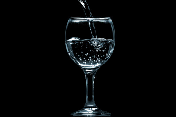 将水倒入黑色背景的玻璃杯中。图片下载