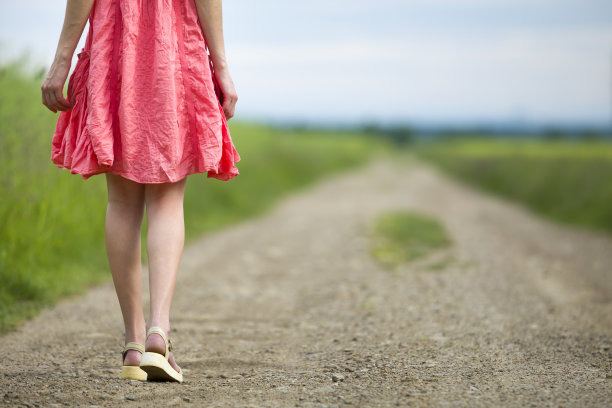 背影的年轻女子在红色的裙子腿走在地面道路上在夏天的一天模糊的阳光背景。图片下载