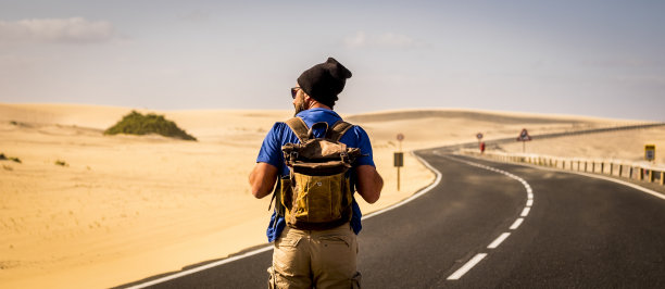 彩色图像的人与旅行背包行走在道路中间与沙丘周围-替代旅行者概念暑假或生活方式的幸福图片下载