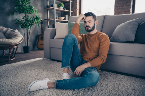 肖像英俊的时髦男子可怕的消息认为不确定的不确定的担心的无意义的坐牛仔牛仔裤橙色的毛衣衬衫套头衫看起来光线的房间触摸手指手前额头运动鞋白色图片下载