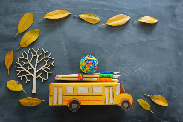 教育与返校理念。顶视图的照片硬纸板校车和铅笔旁边的树与秋天干燥的叶子在教室黑板的背景图片下载